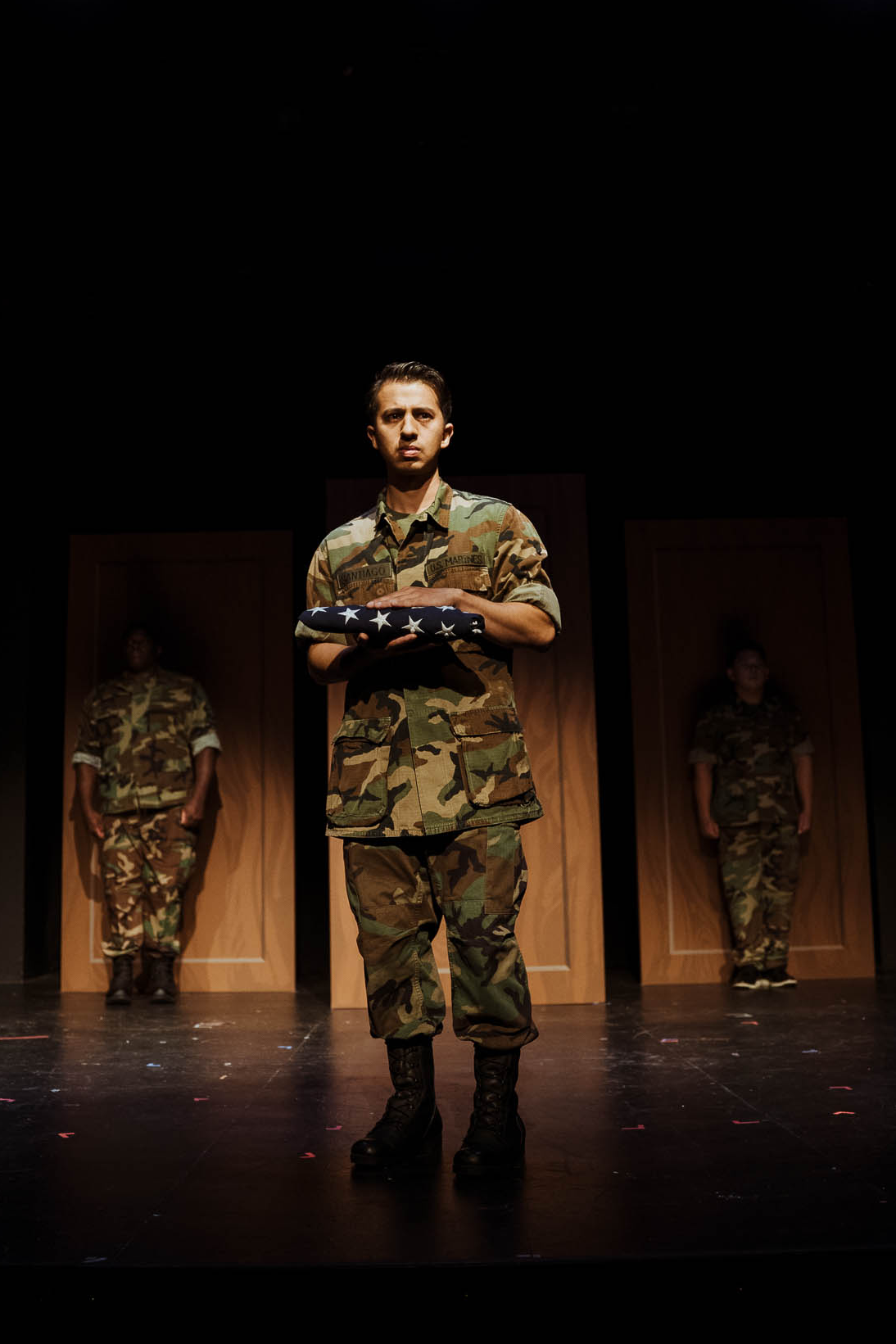 PFC William Santiago holding a folded flag, with two Marines behind him