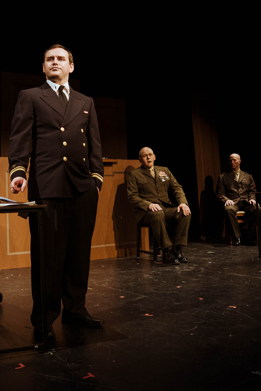 A Navy lawyer standing at the counsel table as two Marine officers look on